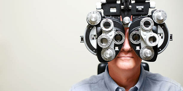Mature man looking through Ophthalmic Instrument called a phoroptor.